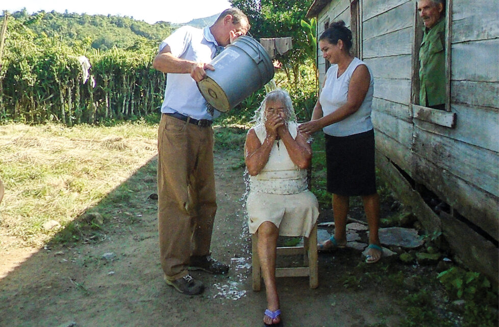 A man pours water over the head of a woman for baptism