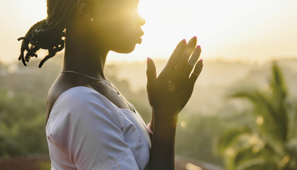 Woman praying with sunset behind her