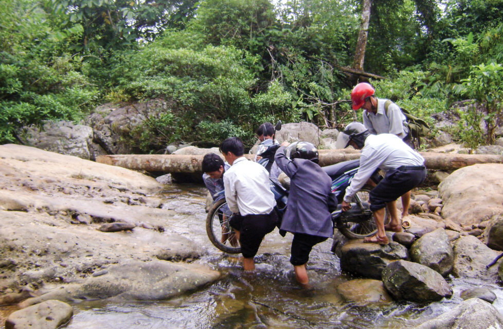 men help carry motorcycle across stream