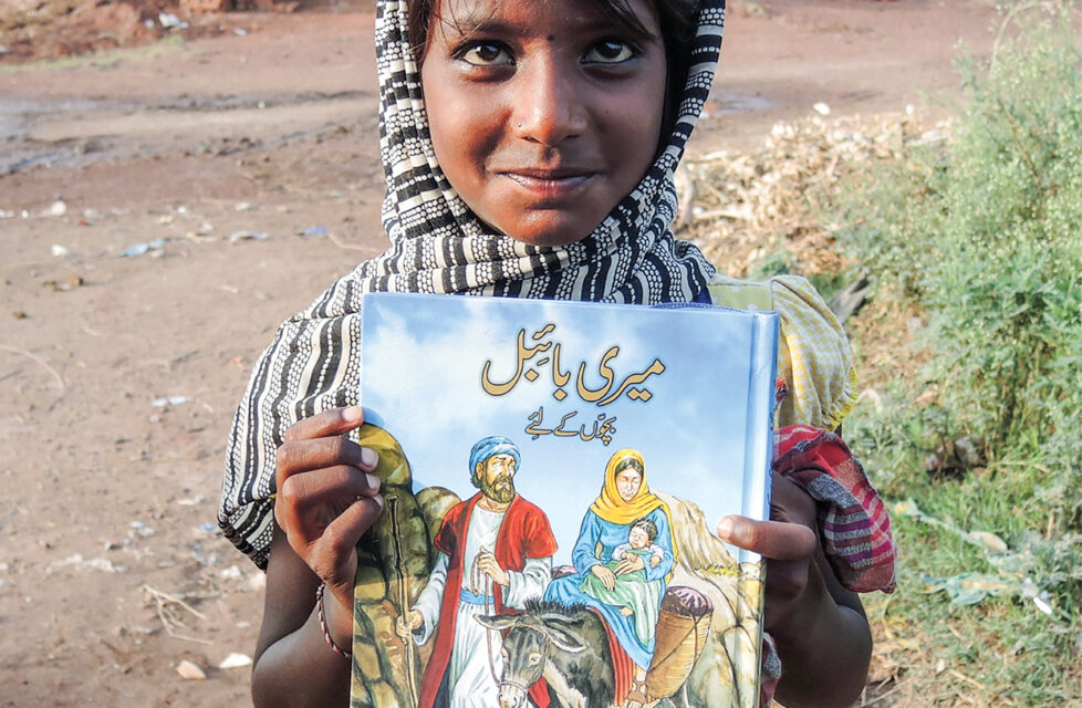Pakistan Bible Smugglers Robbed at Gunpoint Child stands holding a bible and smiling