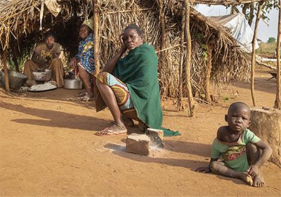 Family sitting in dirt outside straw hut