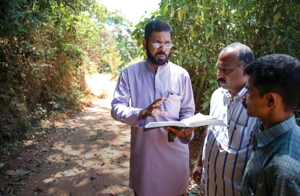 a man reads the bible to two other men outside